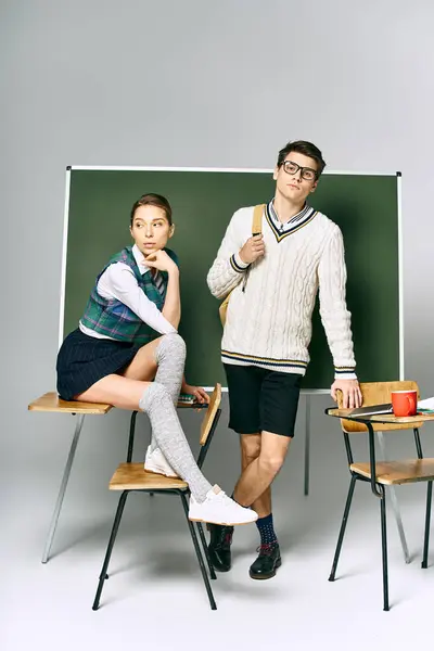 stock image A stylish man and woman posing in front of a green board in a college setting.