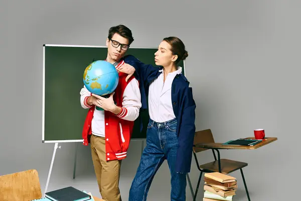 Stock image A male and female students stand in front of a classroom, studying a globe.
