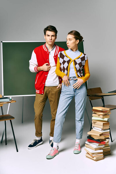 A male and female students pose elegantly in front of a stack of books.