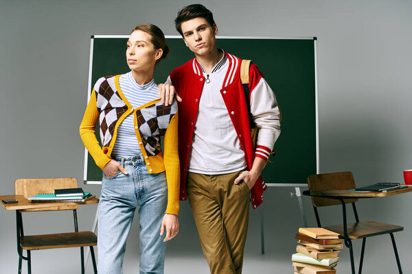 A male and female students in casual clothing posing in front of a green board in a college classroom.