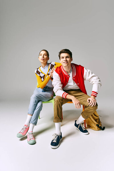 A casually dressed male and female students sitting on a chair in a college classroom, posing coyly.