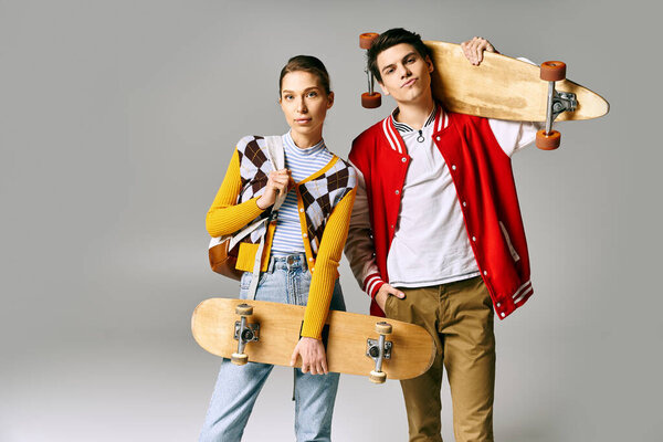 Two young people hold skateboards against a gray backdrop.