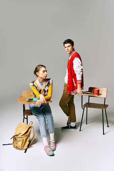Stylish male and female students pose at college desk in casual attire.