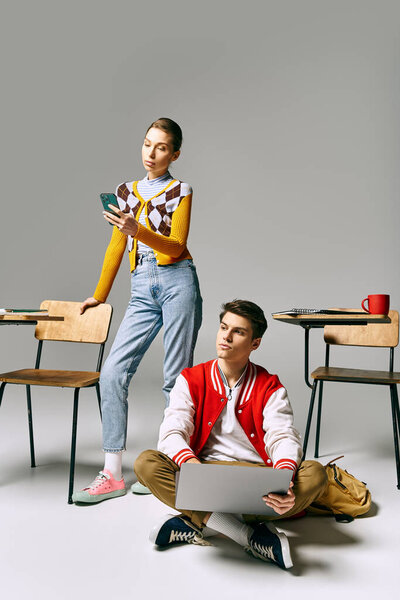 Young male and female students working on a laptop while sitting on the floor in a classroom.