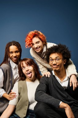 Genç arkadaşlar, koyu mavi arka planda bir grup fotoğrafı için şık kıyafetler içinde birlikte duruyorlar..