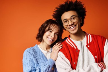 Genç, çok kültürlü bir erkek ve kadın bir stüdyo ortamında şık kıyafetler içinde bir arada duruyorlar..