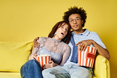 Bir erkek ve bir kadın kanepede oturup patlamış mısırın tadını çıkarıyorlar..