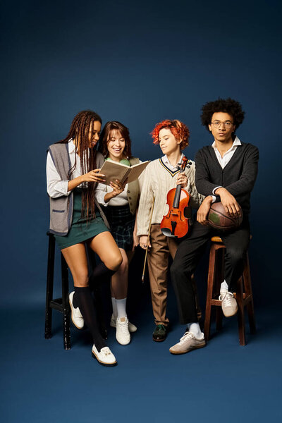 Мультикультурные молодые друзья, сидящие близко в стильной одежде на темно-синем фоне.