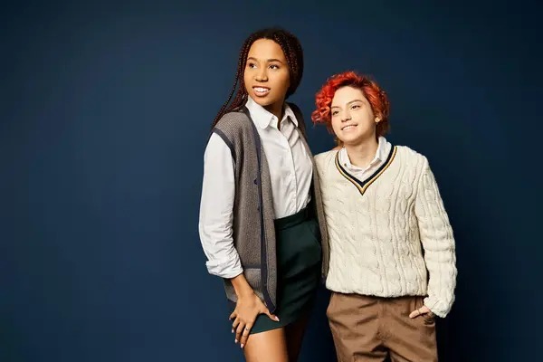 Stock image a woman, along with a nonbinary individual, stand together in stylish attire against a dark blue background.