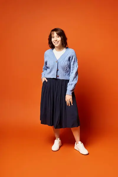 Stock image A woman stands elegantly in front of a vibrant orange background, exuding confidence and grace.