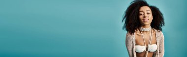 Afro-Amerikalı bir kadın mavi arka planda şık bir mayo giyiyor..
