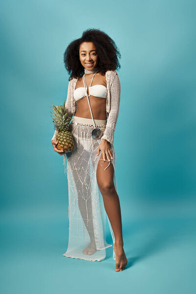 Elegant woman in white swimsuit gracefully holding a pineapple.