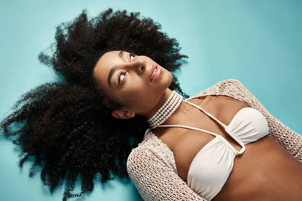 stock image African American woman in trendy bikini lounging on vibrant blue backdrop.