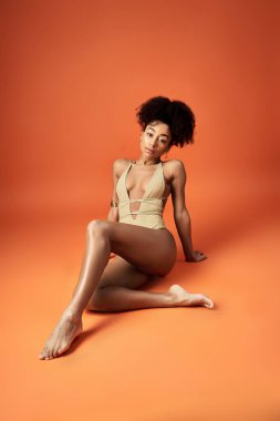 Moda bikinili Afro-Amerikalı kadın canlı turuncu arka planda poz veriyor.