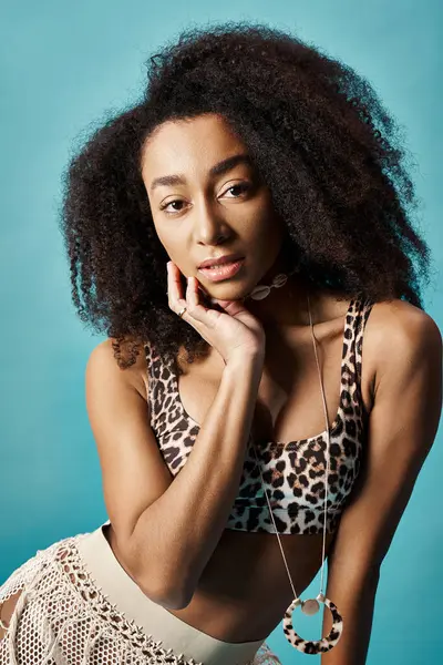 stock image Young African American woman with curly hair striking a pose against a blue backdrop.