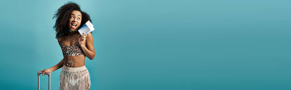 Stylish African American woman in trendy swimsuit holding a suitcase.