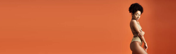 Bikini-clad African-American woman striking a pose against vivid orange backdrop.