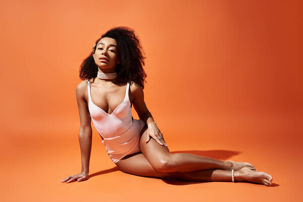 Stylish African American woman in white swimsuit striking a pose against vibrant orange background.