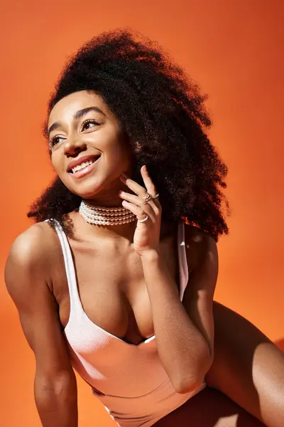 stock image Stylish African American woman in white swimsuit poses on vibrant orange background.