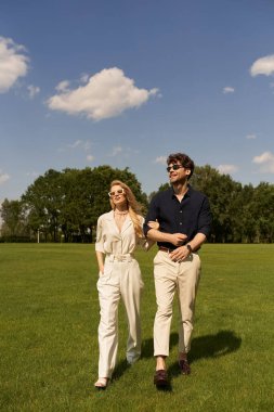 An elegant couple leisurely walks together through a lush green field, exuding old-money sophistication and luxury. clipart