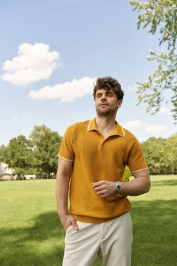 A man in a vibrant yellow polo shirt stands elegantly in a lush green field under the warm morning sun. clipart