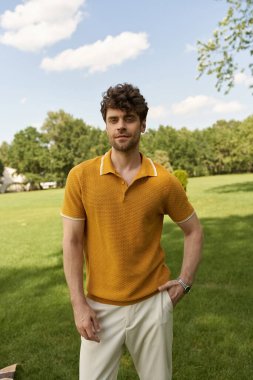 A man in a yellow polo shirt stands elegantly amidst a lush green field under the radiant sun. clipart