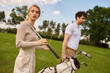 A stylish young man and woman in elegant attire walk leisurely on a lush green golf course, enjoying each others company. clipart