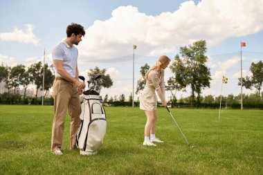 A young couple in elegant attire plays golf on a green field at a prestigious club, enjoying a leisurely day together. clipart