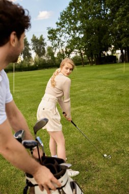 Zarif giyinmiş bir kadın ve bir erkek, lüks bir pistte golf oynayarak, oyunlarından zevk alırken yeteneklerini sergiliyorlar..