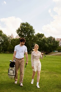 A stylish couple in elegant attire walking together on a lush green golf course under the open sky. clipart