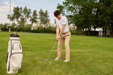 Zarif giyimli bir adam yeşil bir sahada golf sopası sallıyor..