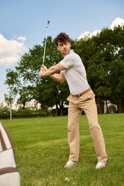 Zarif giyinmiş genç bir adam yeşil bir alanda golf sopası sallıyor, eski paraların lüks yaşam tarzını somutlaştırıyor..