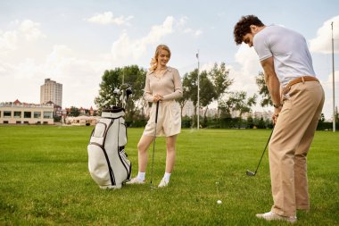 Zarif bir şekilde giyinmiş bir erkek ve kadın, yemyeşil bir alanda lüks bir yaşam tarzını somutlaştıran bir golf turunun tadını çıkarıyorlar..
