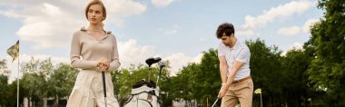 Şık giyinmiş genç bir çift parkta golf oynuyor, yeşil alanda sakin bir günün tadını çıkarıyorlar..