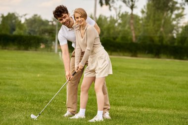 Zarif giyinmiş bir adam ve kadın golf kulübünün yemyeşil sahasında golf oynuyorlar..
