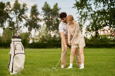Bir adam ve bir kadın şık giyinmiş, golf sahasında golf oynuyorlar..