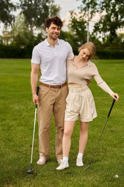Zarif giyinmiş genç bir adam ve kadın açık gökyüzünün altındaki golf sahasında sevgiyle poz veriyorlar..