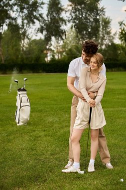 Zarif giyinmiş genç bir çift el değmemiş bir golf sahasının manikürlü sahasında poz veriyor..
