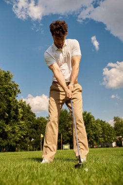 Şık bir adam şık bir şekilde golf topuna vuruyor canlı, çimenli bir alanda, üst sınıfın boş zamanlarının eski para cazibesini somutlaştırıyor..