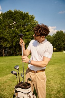 Şık giyinmiş şık bir adam, saygın bir golf kulübünde, yemyeşil bir sahada golf çantası tutuyor. Üst sınıfın eğlencesini somutlaştırıyor..