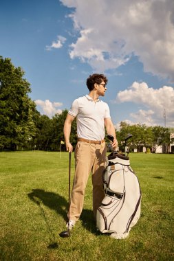 Golf çantasıyla çimenli bir alanda duran bir adam şık bir golf kulübünde üst sınıf bir yaşam tarzını somutlaştırıyor..