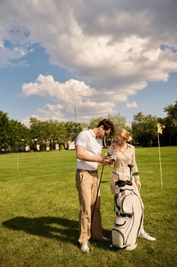 Zarif giyinmiş genç bir çift, yemyeşil bir golf sahasında birlikte eğleniyorlar..
