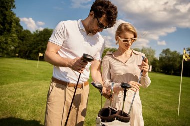 A young couple in elegant attire enjoying a game of golf on a lush green field at a prestigious golf club. clipart