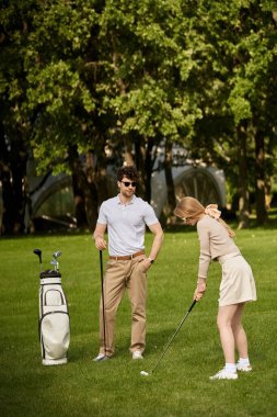 Zarif giyinmiş genç bir çift yemyeşil bir parkta golf oynuyor..