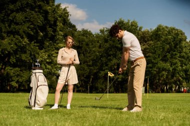 Zarif giyimli genç bir çift, prestijli bir kulübün yemyeşil sahasında golf oynamaktan zevk alıyor. Üst sınıfın boş zamanlarının somut bir örneği..