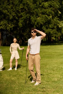 Yeşil bir sahada golf oynayan zarif giyinmiş genç bir çift birlikte sakin bir günün tadını çıkarıyor..