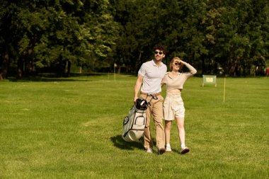 A stylish young couple takes a leisurely walk on a picturesque golf course, enjoying each others company. clipart