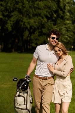 Bir adam ve bir kadın zarif bir şekilde poz vererek yemyeşil bir golf sahasında sofistike bir günün tadını çıkarıyorlar..
