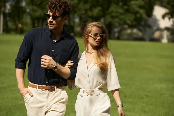 stock image A stylish, well-dressed man and woman leisurely walk in a lush park, embodying a classic, affluent lifestyle.