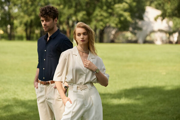 A stylish man and woman in elegant attire in a lush green park, exuding a sense of luxury and romance.